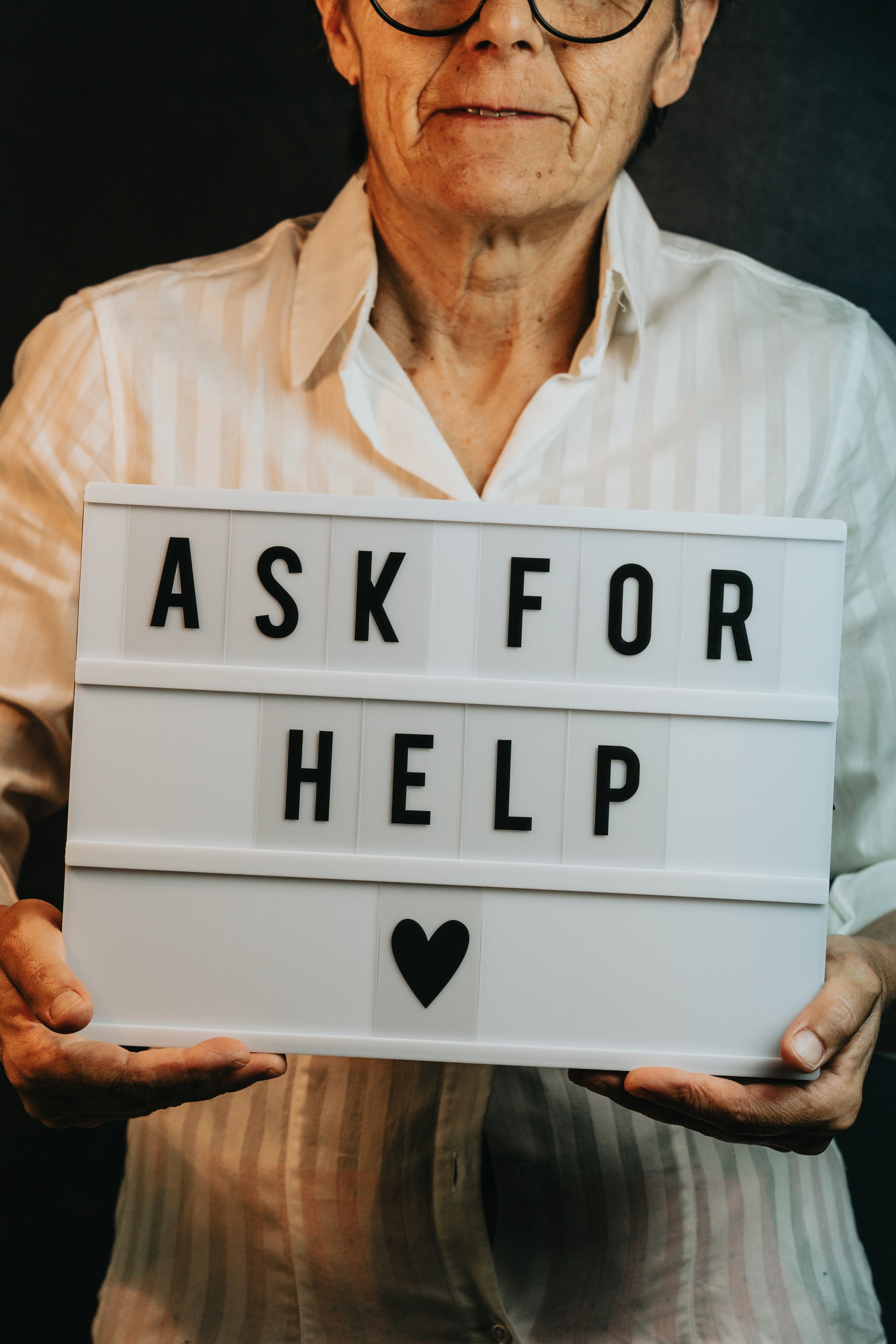 An old man holding an Ask for Help sign