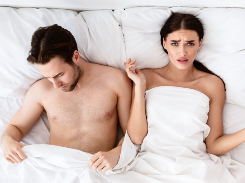 Disappointed looking woman in bed next to her partner illustrating the emotional impact of erectile difficulty