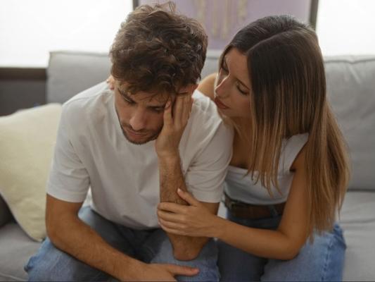 Female partner comforting male partner on a couch