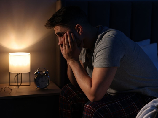 Man sitting alone on the edge of a bed at night looking stressed and withdrawn